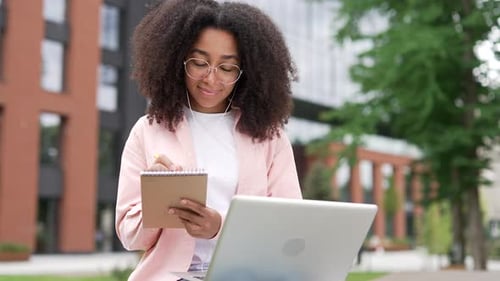 Afroamerikanische Studentin hört sich den Online-Videokurs mit einem Laptop auf der Bank an