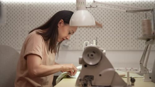 Focused Seamstress Stitching Fabric on Sewing Machine in Atelier Under Bright Workshop Lighting Side