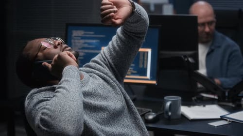 Cybersecurity Analyst on Phone Reviewing Code on Computer during Night Shift