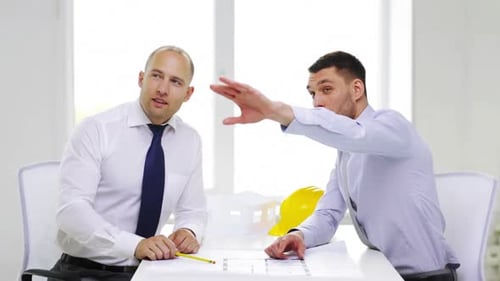 Successful businessmen smiling and discussing a project blueprint in the office