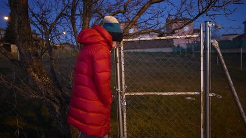 Woman in Red Jacket Struggles to Open Locked Chain Fence Gate at Night