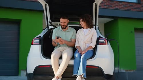 Couple Talking and Using Smartphone While Charging Electric Car