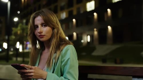 Stylish Woman Using Phone at Night on Bench