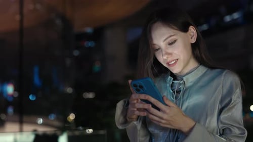 Attractive Girl Standing Outside in the Night Street and Scrolling Pictures in the Gallery for