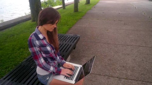 Woman Works on Laptop at Lakeside Park Bench