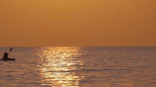 Dark Silhouette of Lonely Fisherman Rowing on His Boat on Sea Water at Sunset