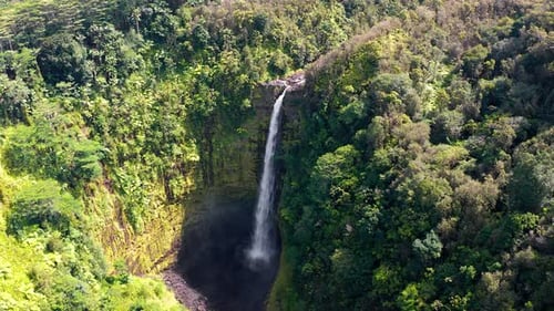 Towering rainforest waterfall plunging into deep volcanic basin from aerial view
