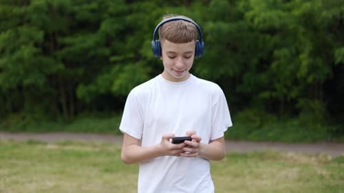 Teen Listens to Music on Headphones in Park