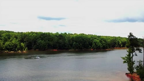 A boat circling in the river with the camera rising above the trees.