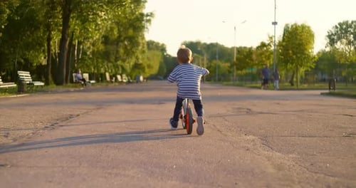 A Child Boy Rides Balance Bike in a City Park