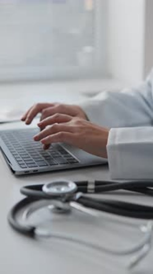 Person Typing on Laptop with Stethoscope on Desk