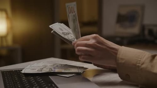 Hands Counting Money by Laptop Indoors
