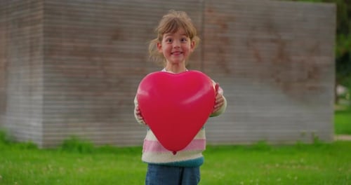 Little Girl Holding a Red Heart Balloon Outdoors