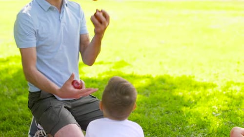Man Juggling Apples for a Child in Park