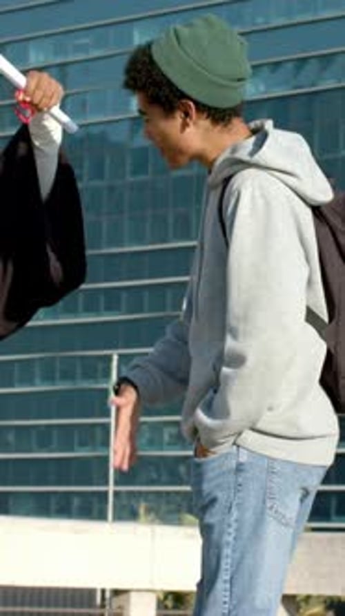 Vertical video: Extending graduate diploma, beanie man reaching and giving congrats at plaza
