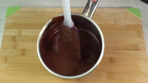Rühre heiße Schokolade in einem Topf mit einem Küchenspatel von Hand um, um ein Dessert zuzubereiten.
Kochen