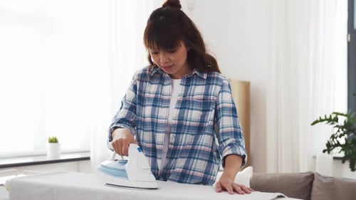 Woman ironing clothes on ironing board in living room