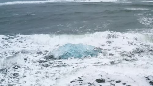 Stunning drone shot of waves breaking on a beautiful ice rock at Diamond Beach in Iceland (slow moti