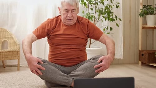 Hombre mayor maduro feliz haciendo ejercicios de gimnasia en casa en línea con una computadora portátil, un estilo de vida saludable