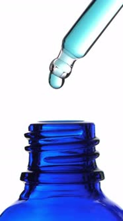 Drop of Liquid Falling From Glass Lab Pipette in Transparent Bottle Isolated on White Background