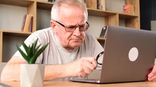 Senior Man Inspecting Laptop with Magnifying Glass