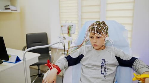 Serious teenage boy wearing sensors on his head and special clips on the wrists.