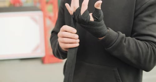Closeup View of a Strong Boxer Man Putting on Black Boxer Bands in the Outdoor Gym Work Out