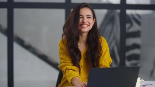 Smiling businesswoman laughing at funny message on laptop in modern office