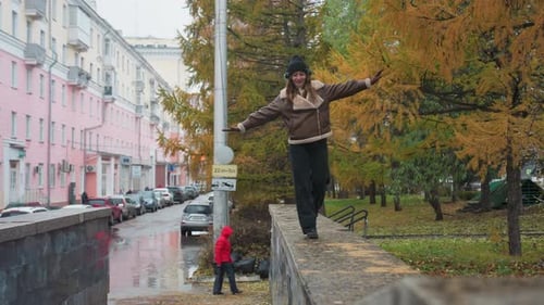 Smiling Girl Walking on Stone Path in Drizzling Rain with Outstretched Arms