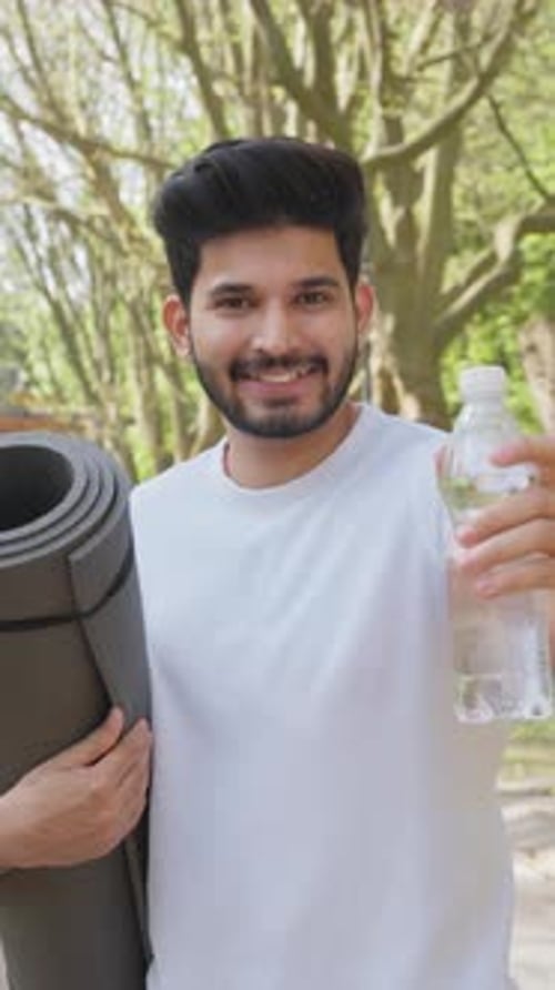 Young Man Holding Water Bottle Outdoors with Yoga Mat