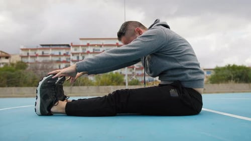 Sporty Athlete Man Does Stretching While Sitting In Sports Field