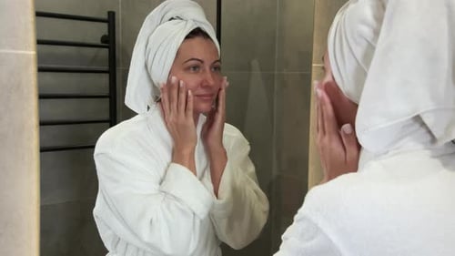 Blonde Woman Applying Lotion to Face in Bathroom