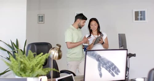 Discussing project, colleagues using tablet and computer in modern office setting