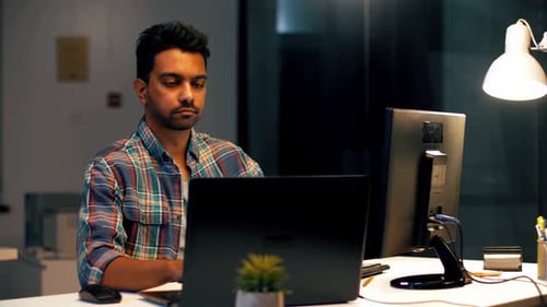 Junger Inder arbeitet spät in der Nacht über Stunden im dunklen modernen Büro auf einem Laptop