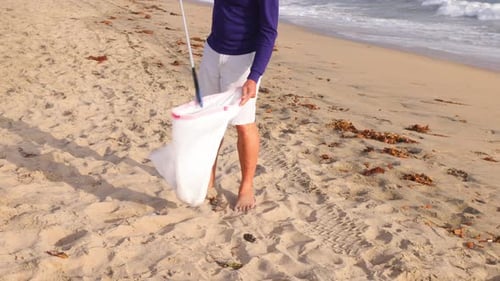 Mature Man Picking Up Trash At The Beach