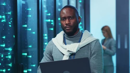 A Man Works Diligently on a Laptop in a Server Room Focused