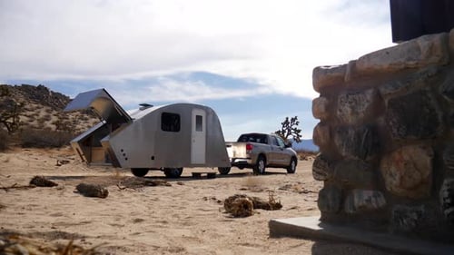 Reveal of a metal teardrop travel trailer tiny house towed by a pickup truck parked at a desert camp