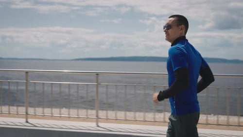 A Young Athletically Built Young Man Runs Along a Wellmaintained Embankment Workout to Keep Fit and