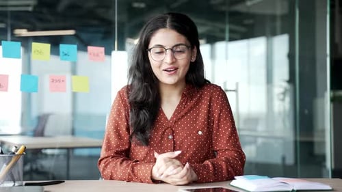 Webcam view. Young businesswoman talking on a video call looking at camera sitting at a workplace