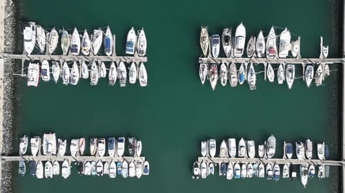 Drone bird's eye view descends on sailboats, yachts, and fishing vessels docked at new concrete pier