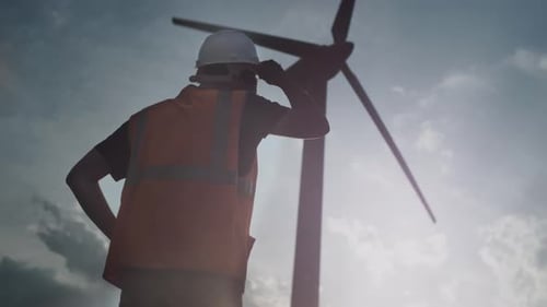 A Male Engineer or Repair Worker Stands Next to a Wind Turbine Man Looks at the Propeller and Fan