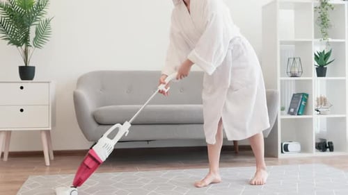 Woman in Robe Vacuuming the Living Room Carpet