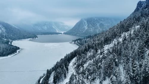 Tranquil scenery of the mountains covered with pine tree woods. Large lake is covered with the ice.
