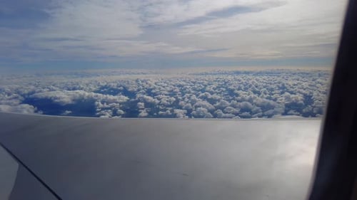 Dynamic view of airplane wing flying and tilting above beautiful cotton-like clouds