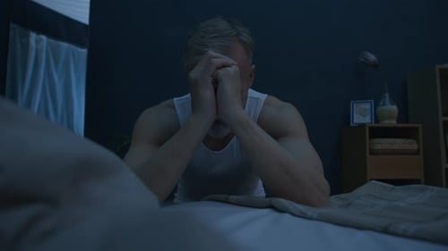 Man Sitting on Edge of Bed at Night