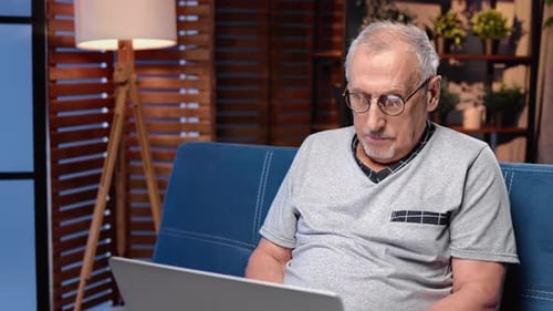 Senior Man Typing on Laptop on Blue Couch