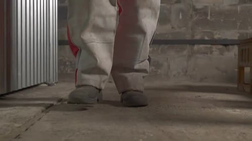 Worker in Protective Pants Walks Along Empty Plant Workshop