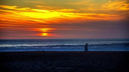 Golden sunset ocean time lapse with people walking along the beach in silhouette