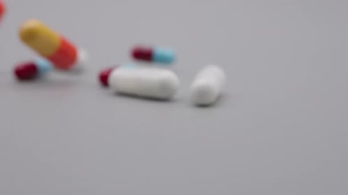 SLOW MOTION SHOT OF PILLS ROLLING DOWN A GREY SURFACE