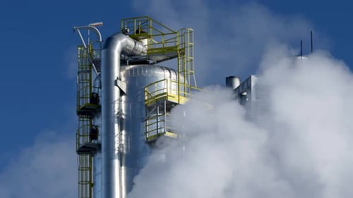 Torre de tanques de acero en una refinería química cubierta de humo contra el cielo azul